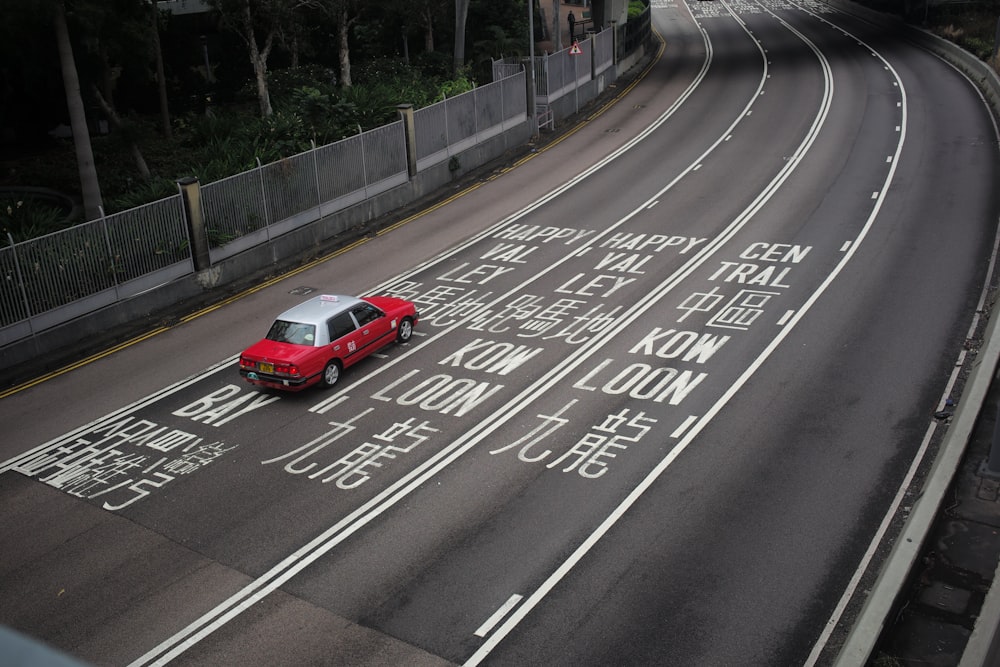 a red car driving down a street next to a bridge