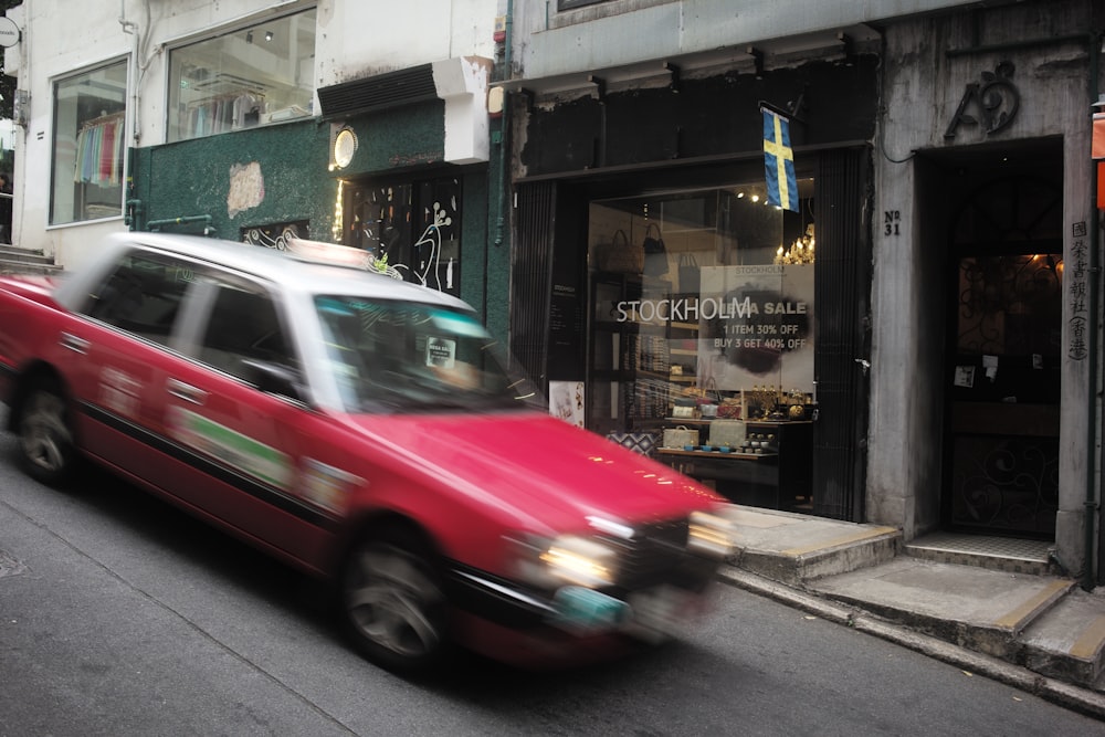 a red car driving down a street next to tall buildings