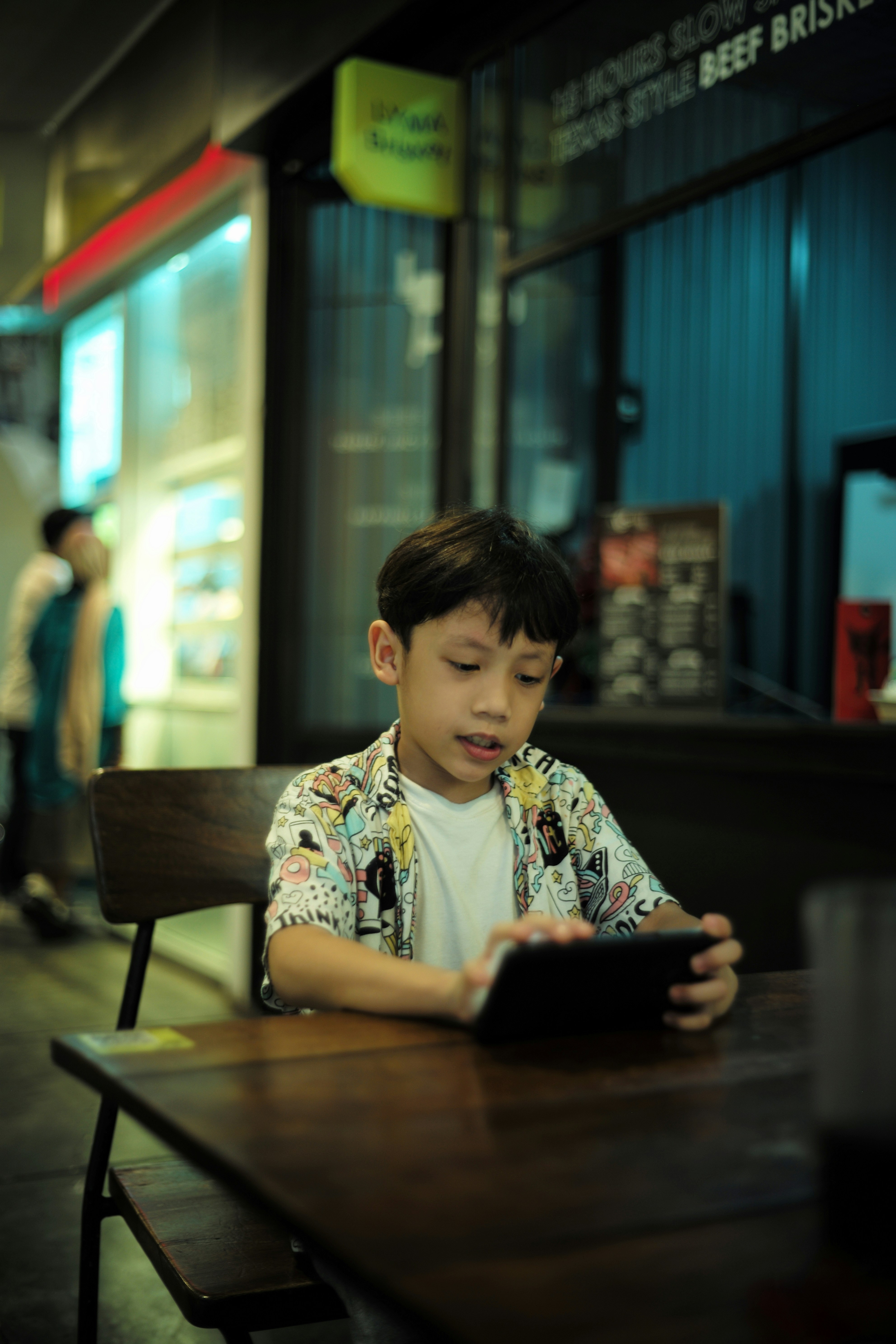 a young boy sitting at a table using a tablet