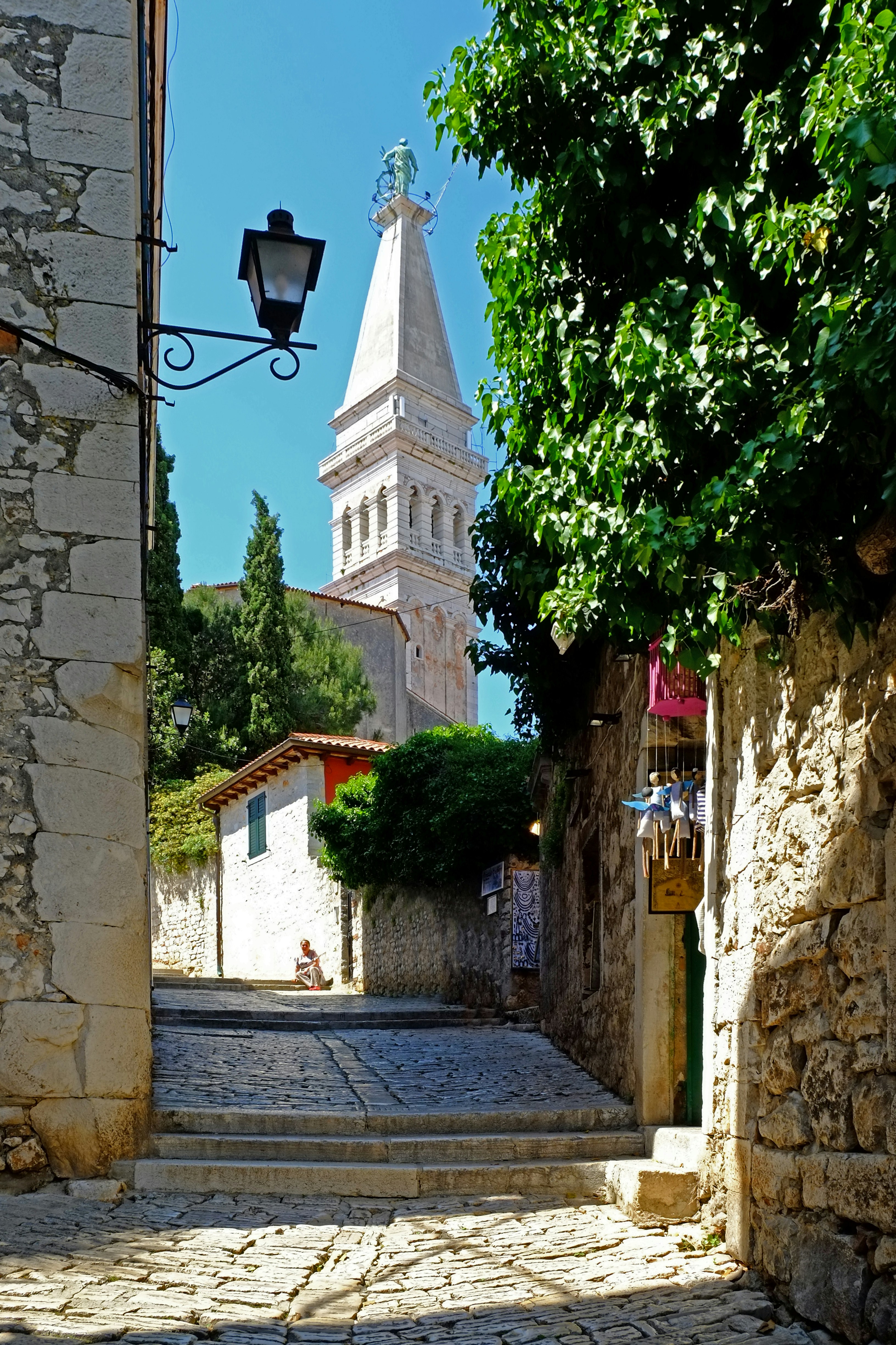 Strada acciottolata con edifici in pietra e campanile.