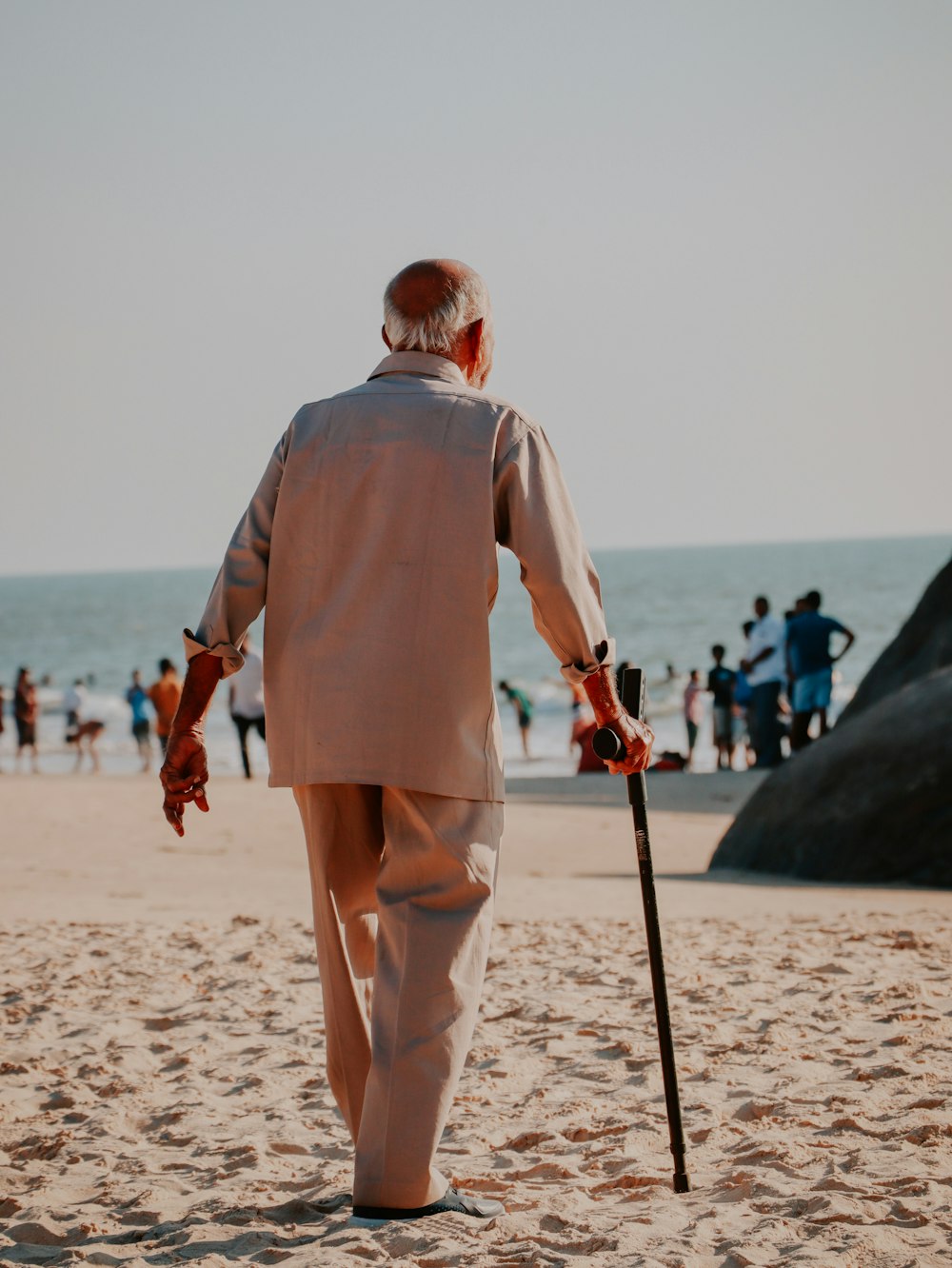 a man walking on the beach with a cane