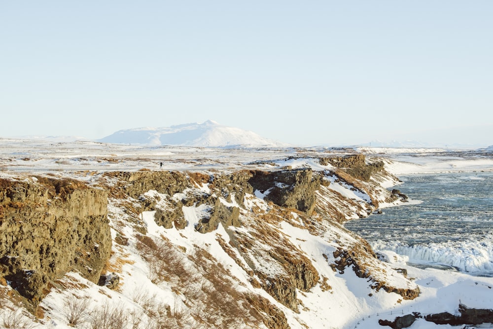 a man standing on top of a snow covered cliff next to the ocean