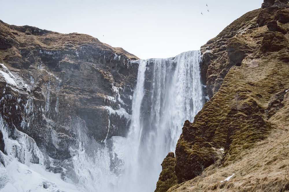 a large waterfall with snow on the ground