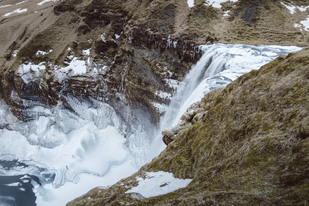 a man standing on top of a snow covered mountain next to a waterfall