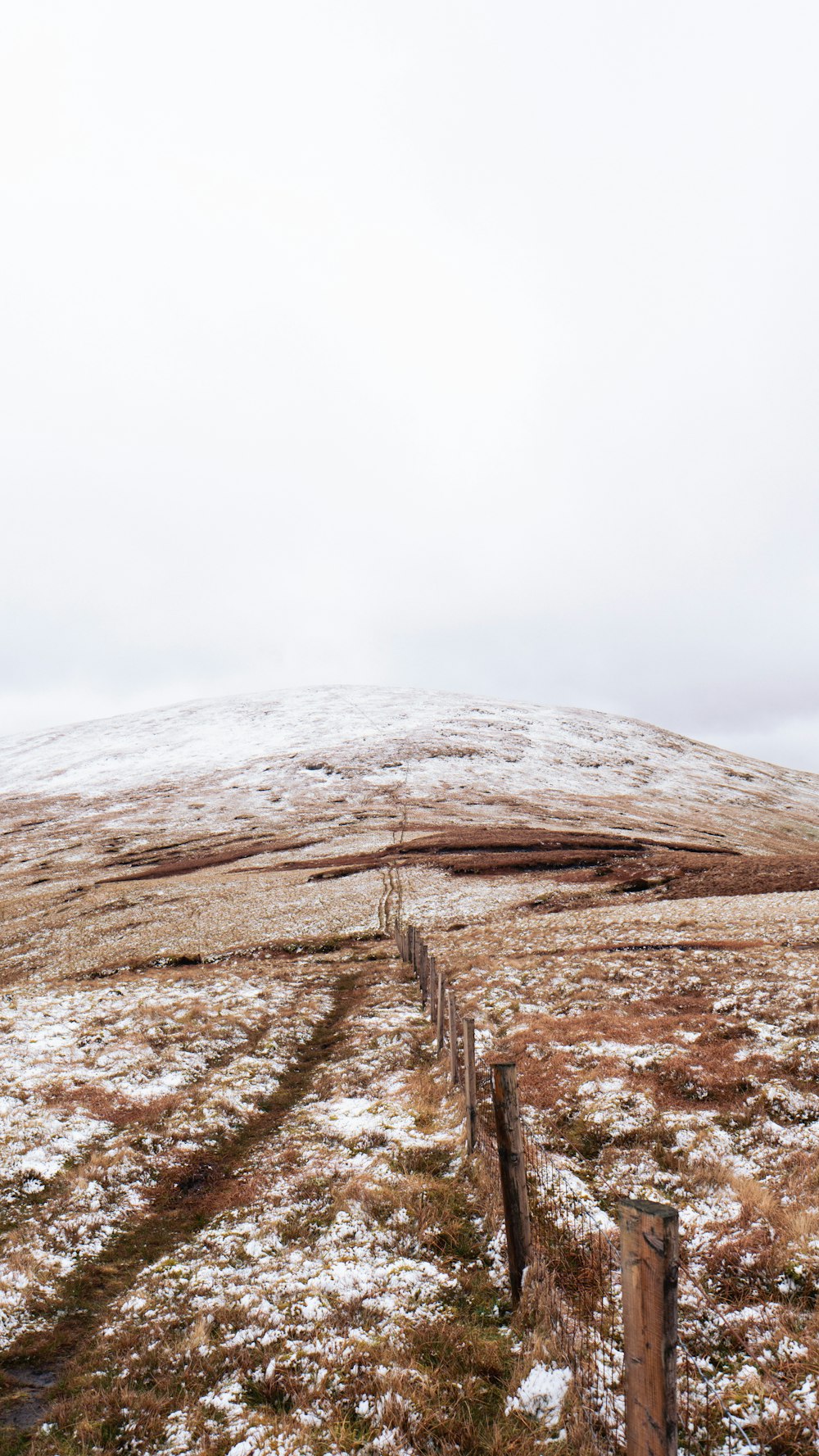 a snowy field with a fence and a hill in the background