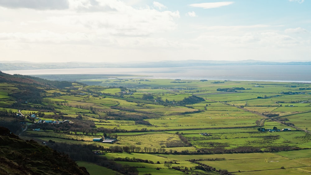 a scenic view of a green valley with a body of water in the distance