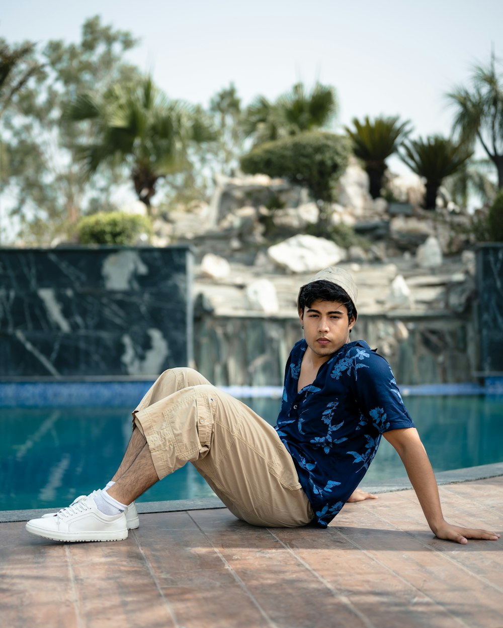 a man sitting on the ground next to a swimming pool