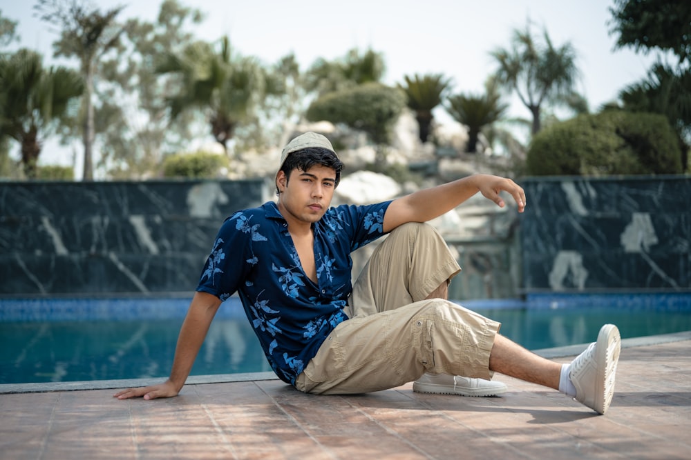 a young man sitting on the ground next to a swimming pool