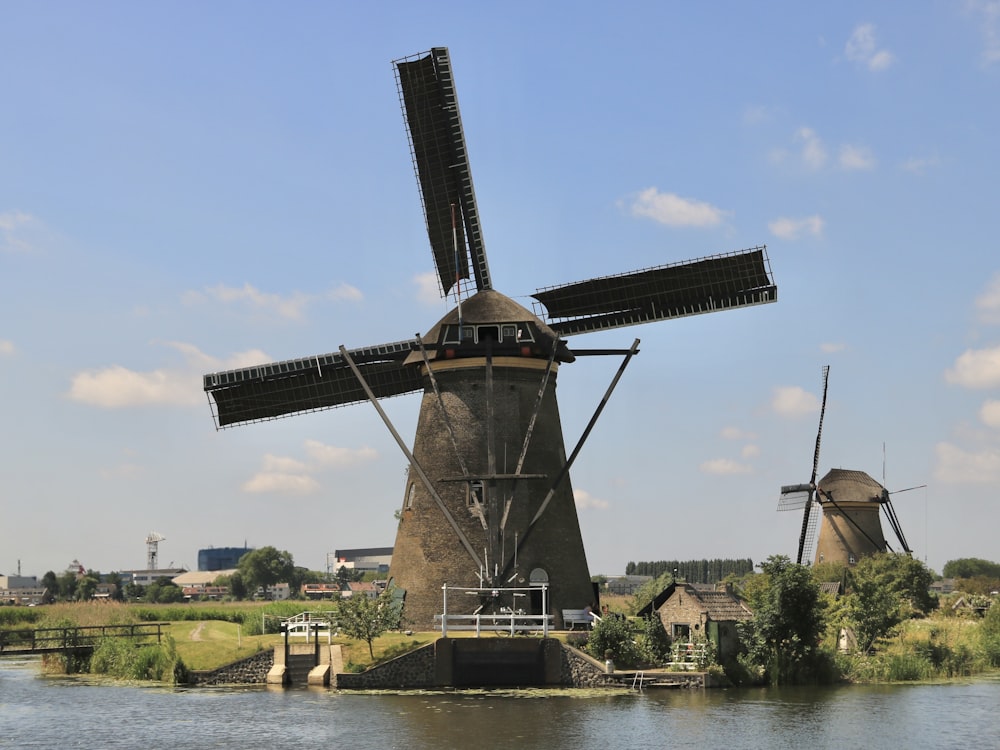 a windmill sitting on top of a river next to a lush green field