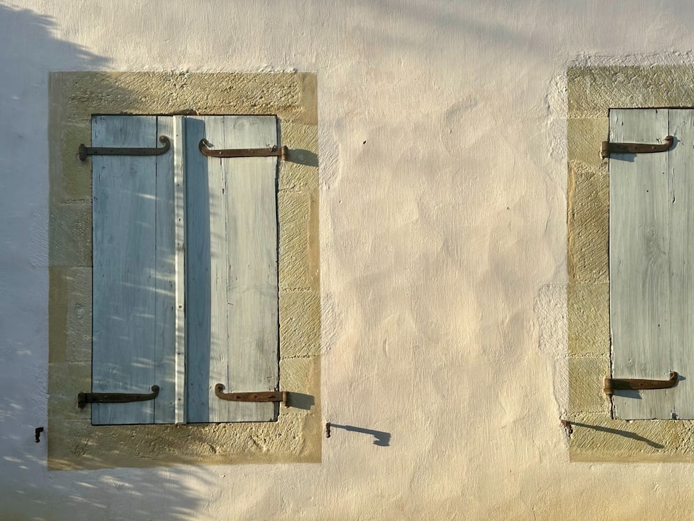 two windows with blue shutters on a stucco wall