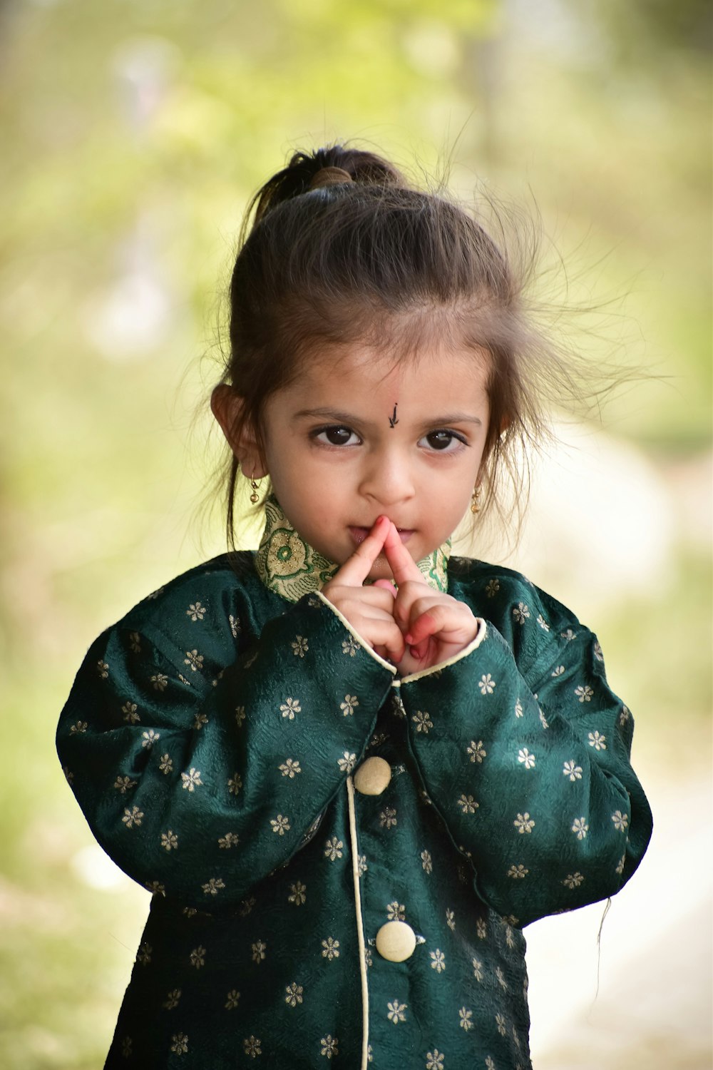 a little girl standing in the woods with her finger on her mouth