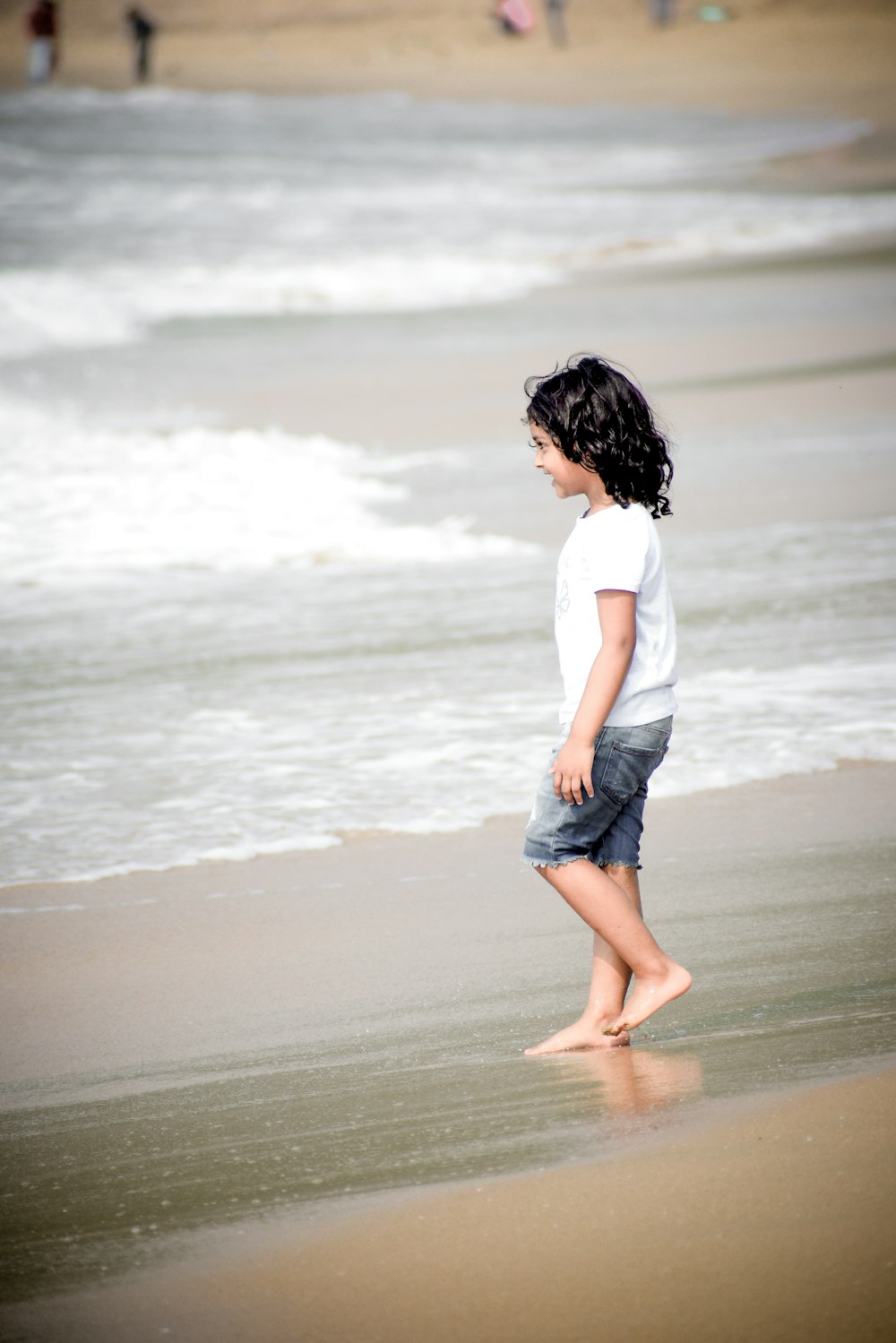 a little girl walking along a beach next to the ocean