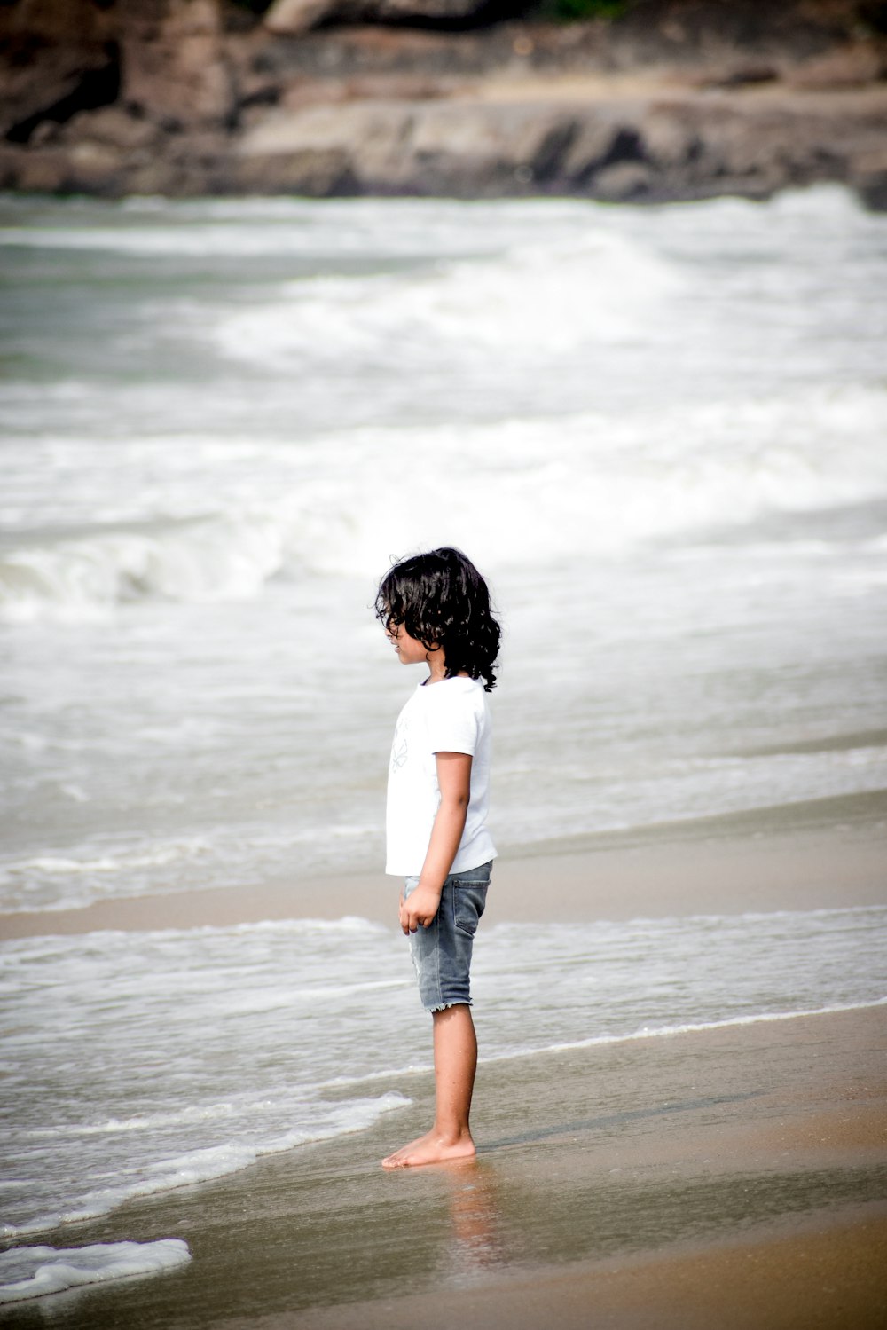 a little girl standing on top of a sandy beach