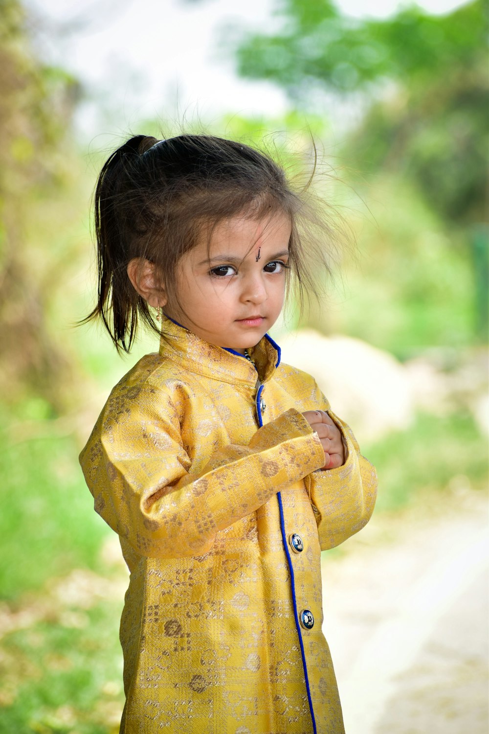 a little girl in a yellow jacket standing on a dirt road