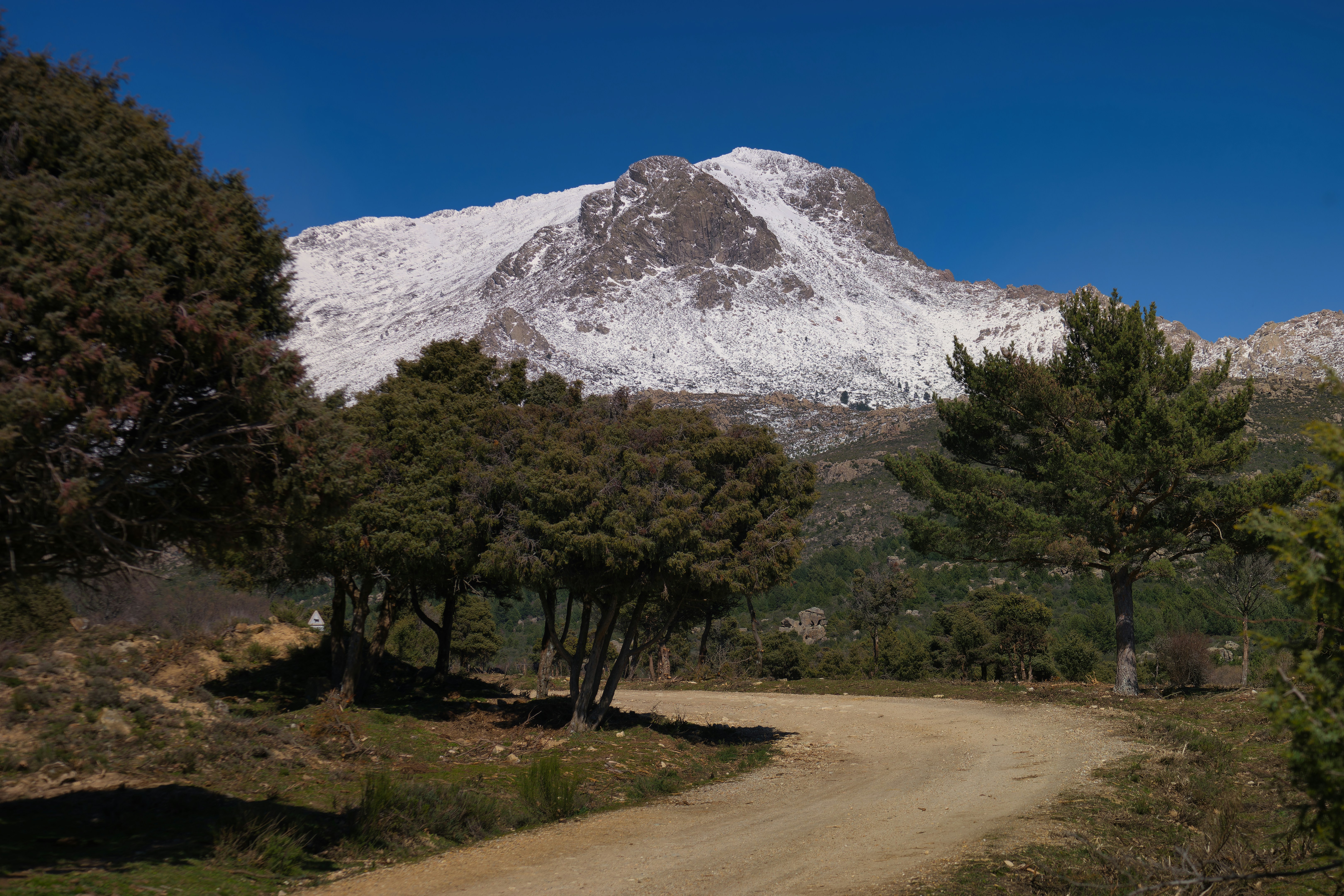 a dirt road in front of a snow covered mountain