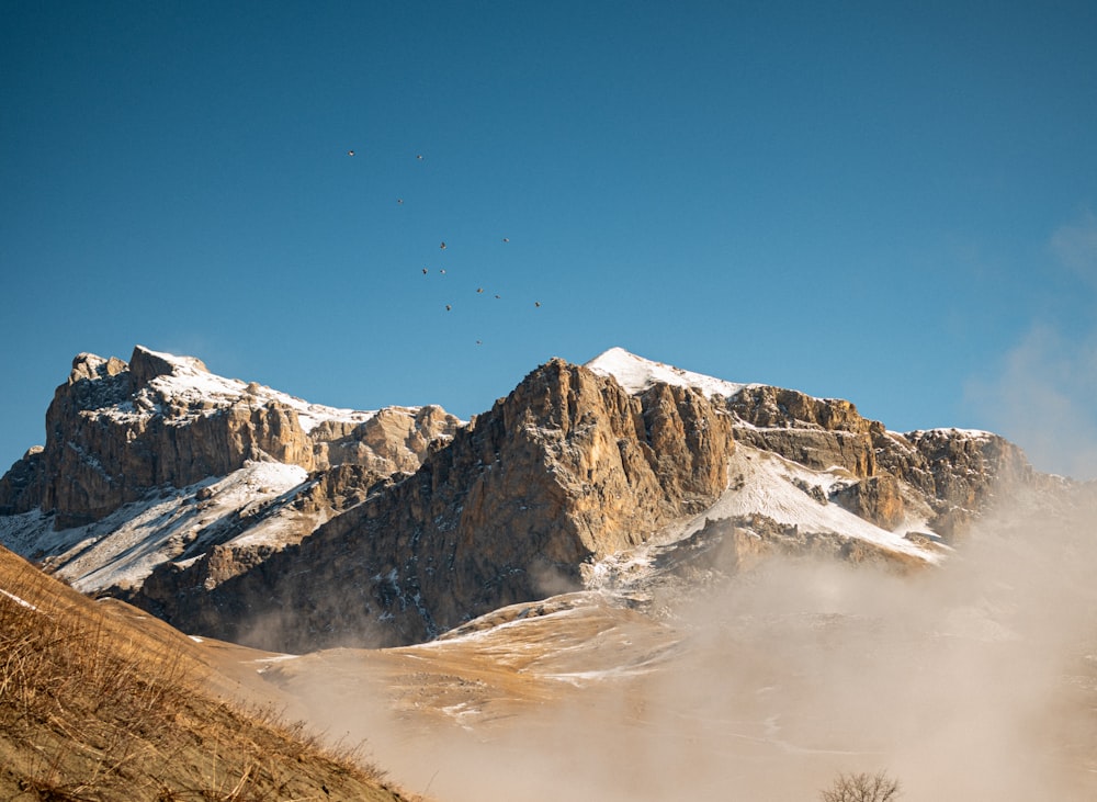 a snow covered mountain with birds flying in the sky