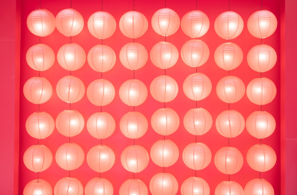uma parede vermelha com um monte de lanternas brancas penduradas nela