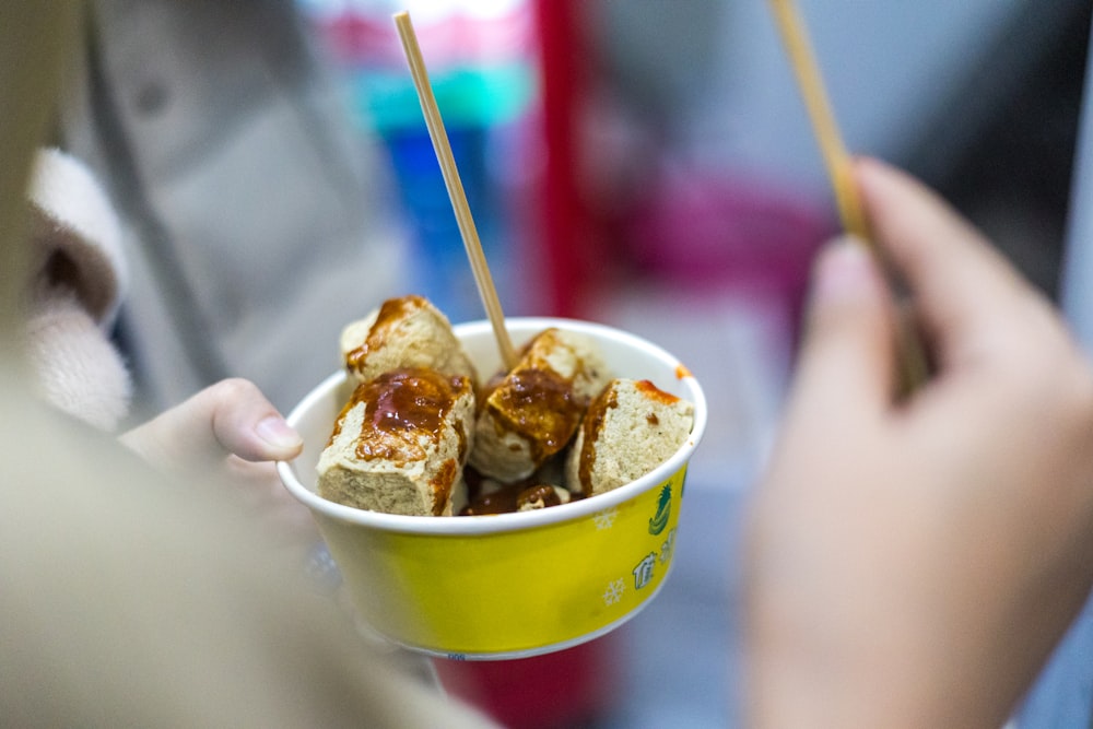 a person holding a yellow cup filled with food