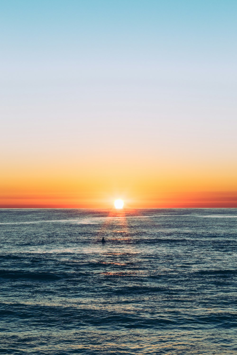 the sun is setting over the ocean with a boat in the water