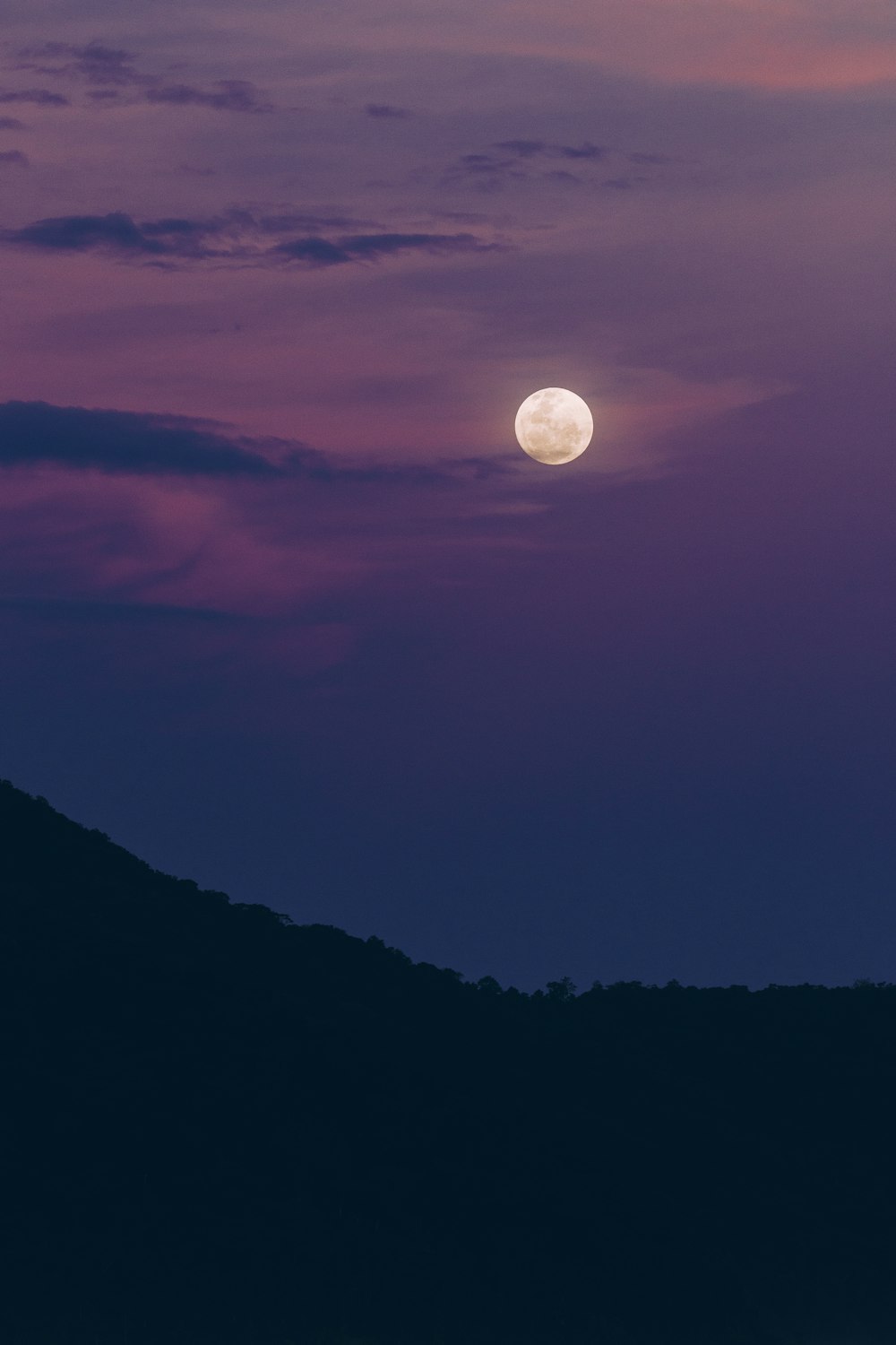 the moon is setting over a mountain range