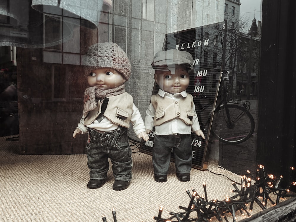 un par de muñecas que están de pie frente a una ventana