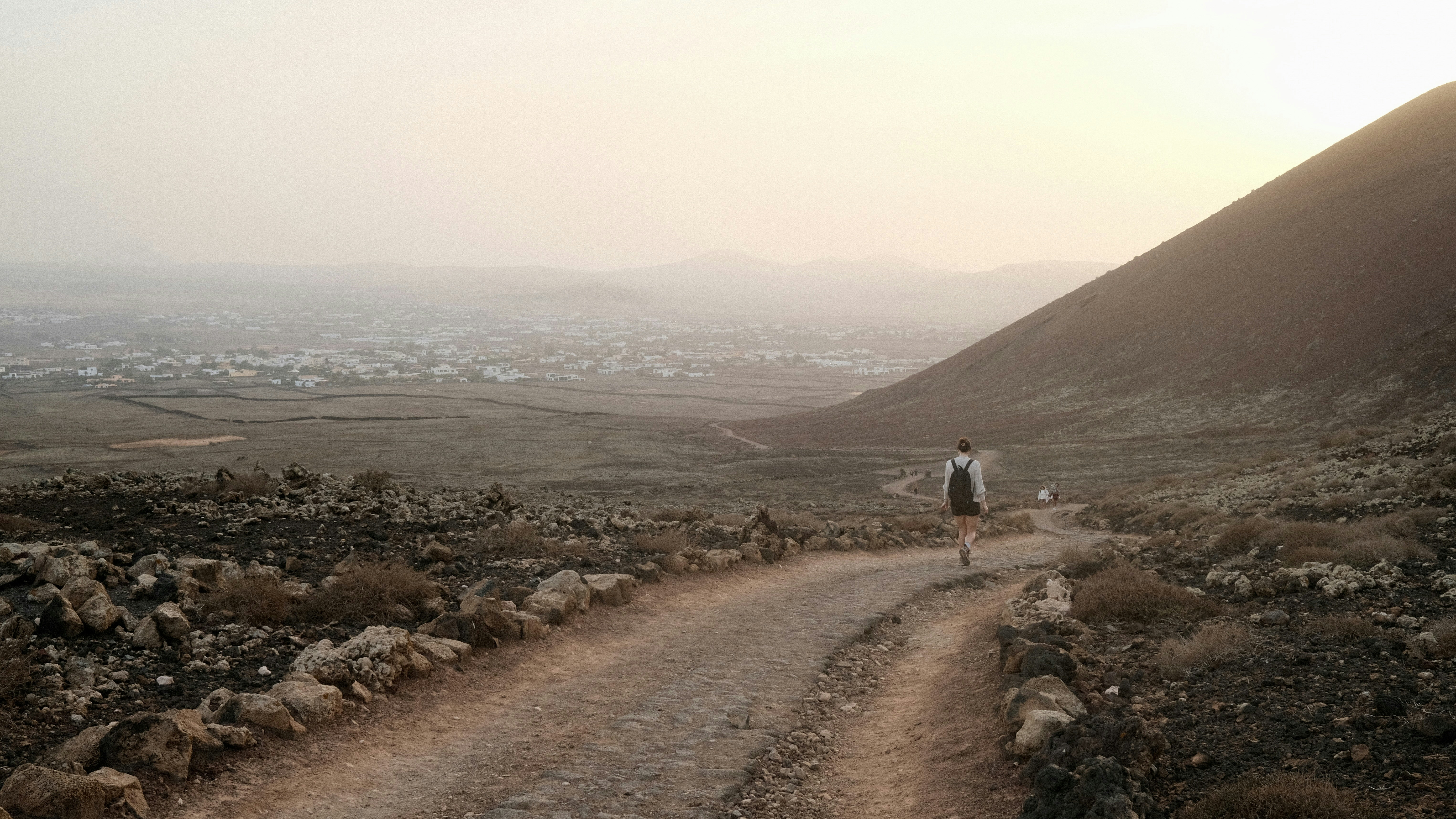 a man walking down a dirt road next to a mountain