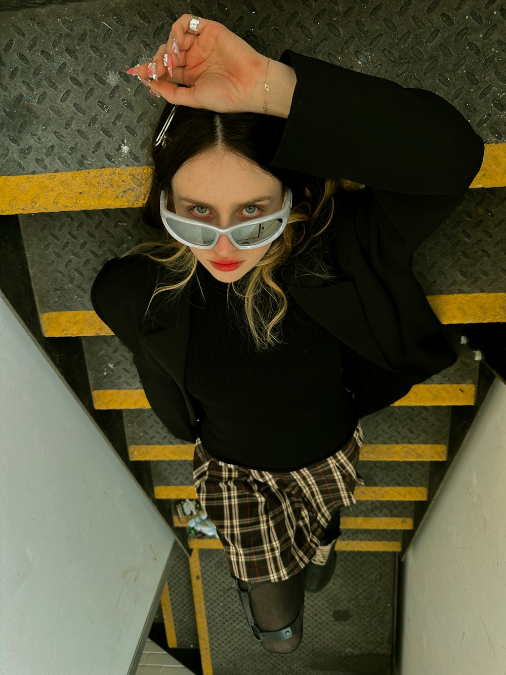 a woman in a black shirt and plaid skirt holding a pair of sunglasses