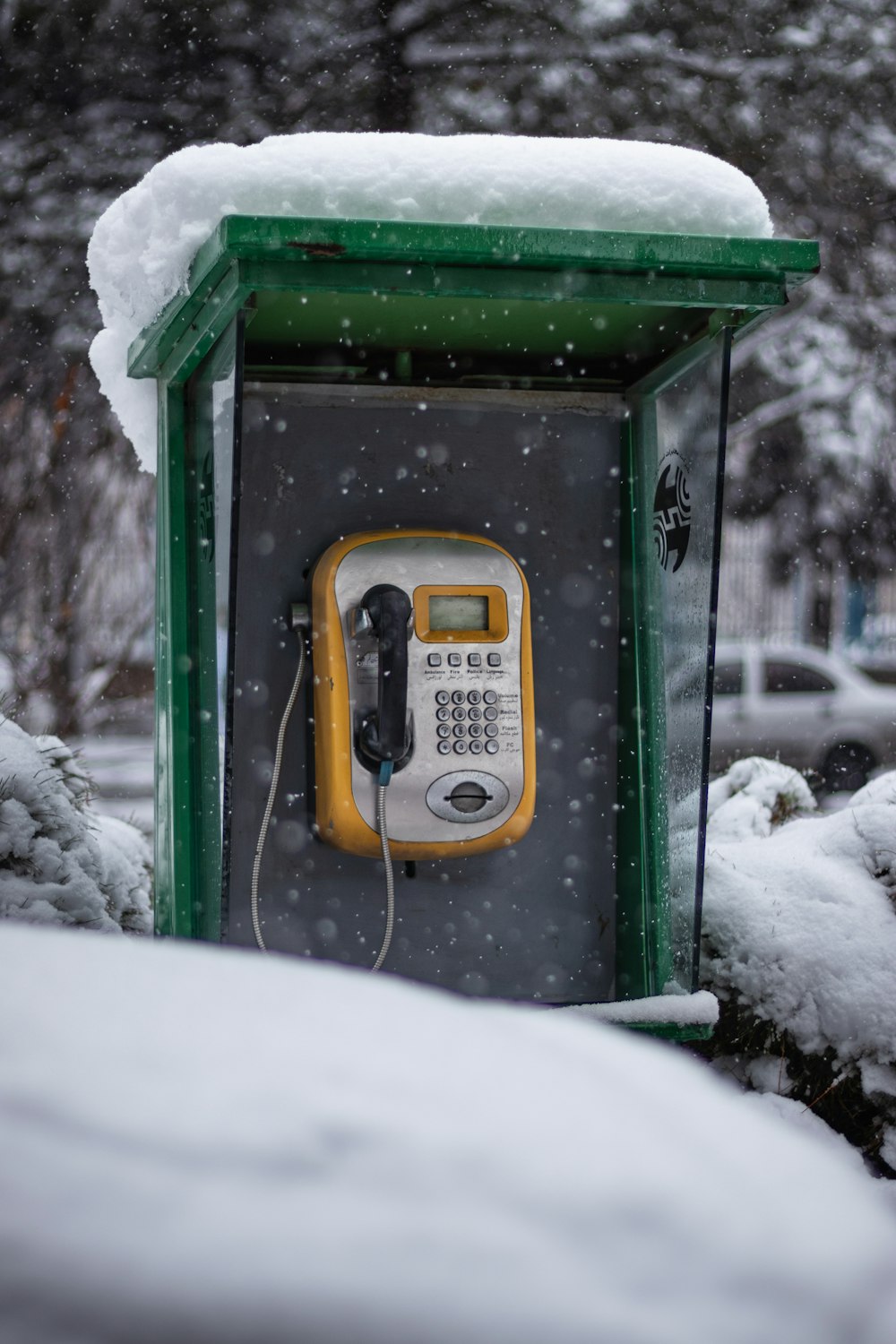 a phone booth covered in snow next to a tree