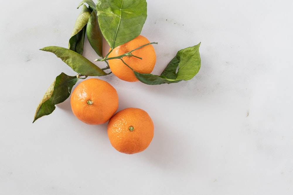 three oranges with green leaves on a white surface
