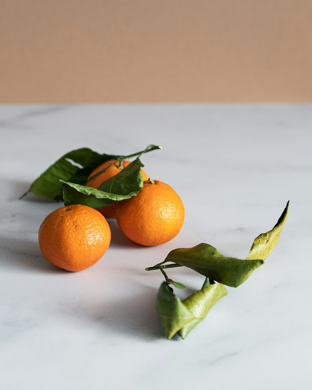 three oranges with leaves on a marble table