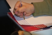 a person writing on a piece of paper with a pen