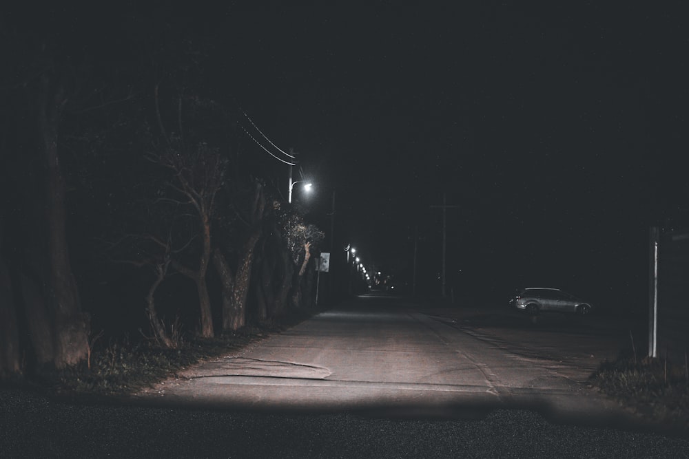 a dark street at night with a car parked on the side of the road