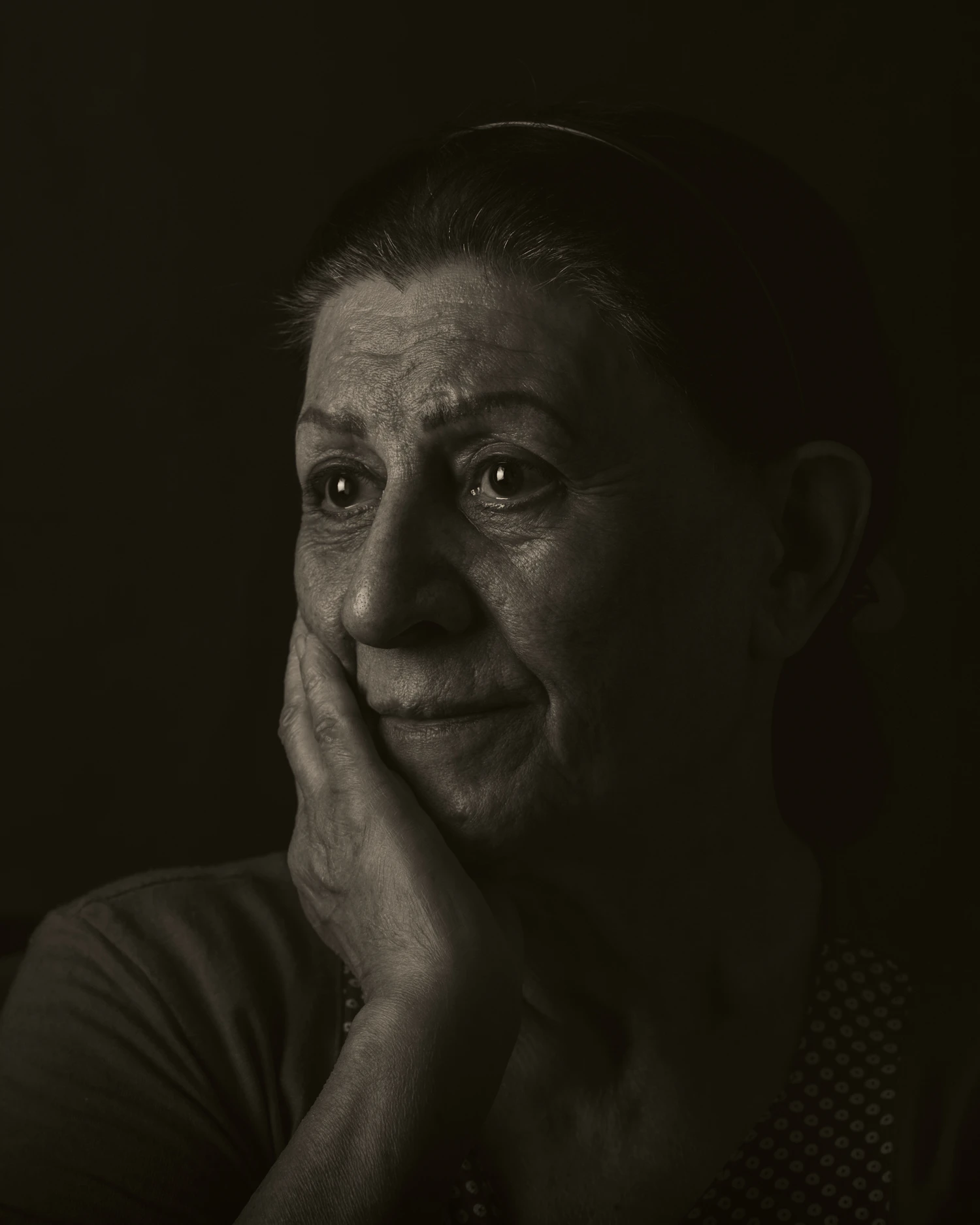 An older woman resting her cheek on her hand in low light