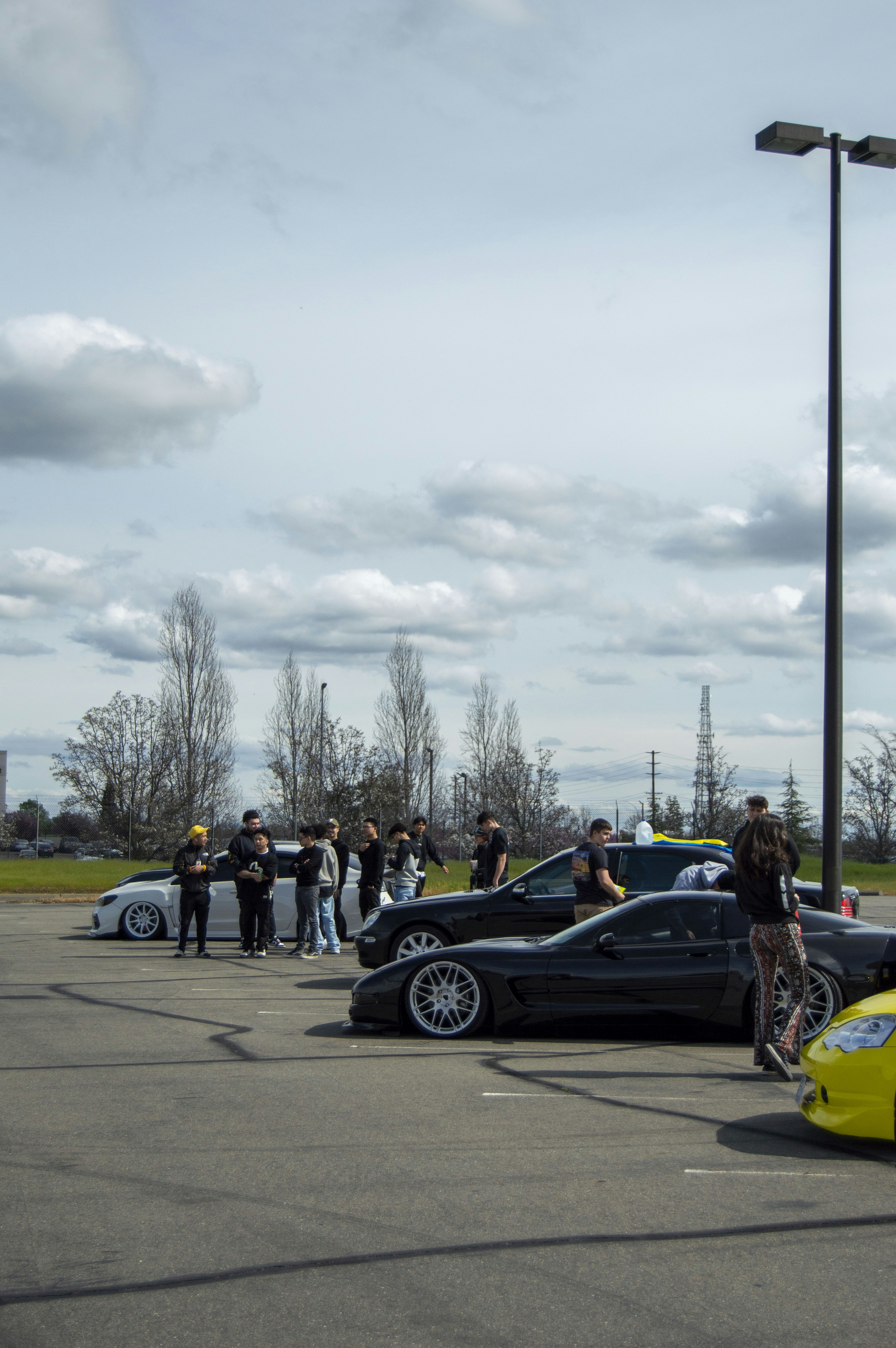 A group of people standing in a parking lot next to parked cars