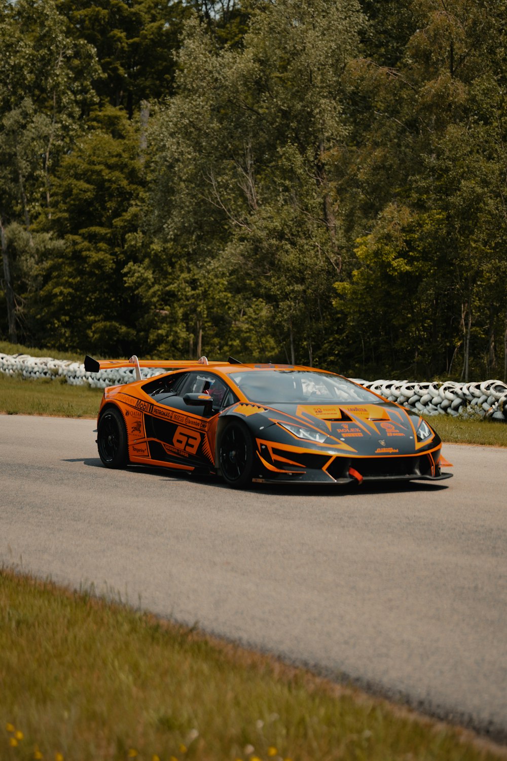 an orange and black sports car driving down a road