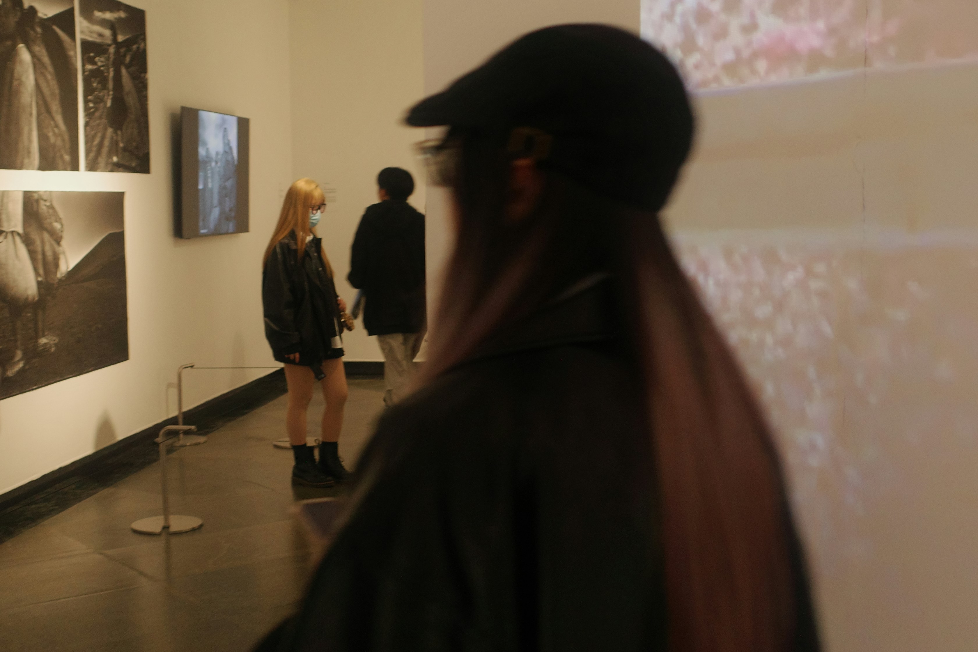 Contemporary art exhibition gallery, dim atmospheric lighting, white walls with large paintings, low-key ambient light