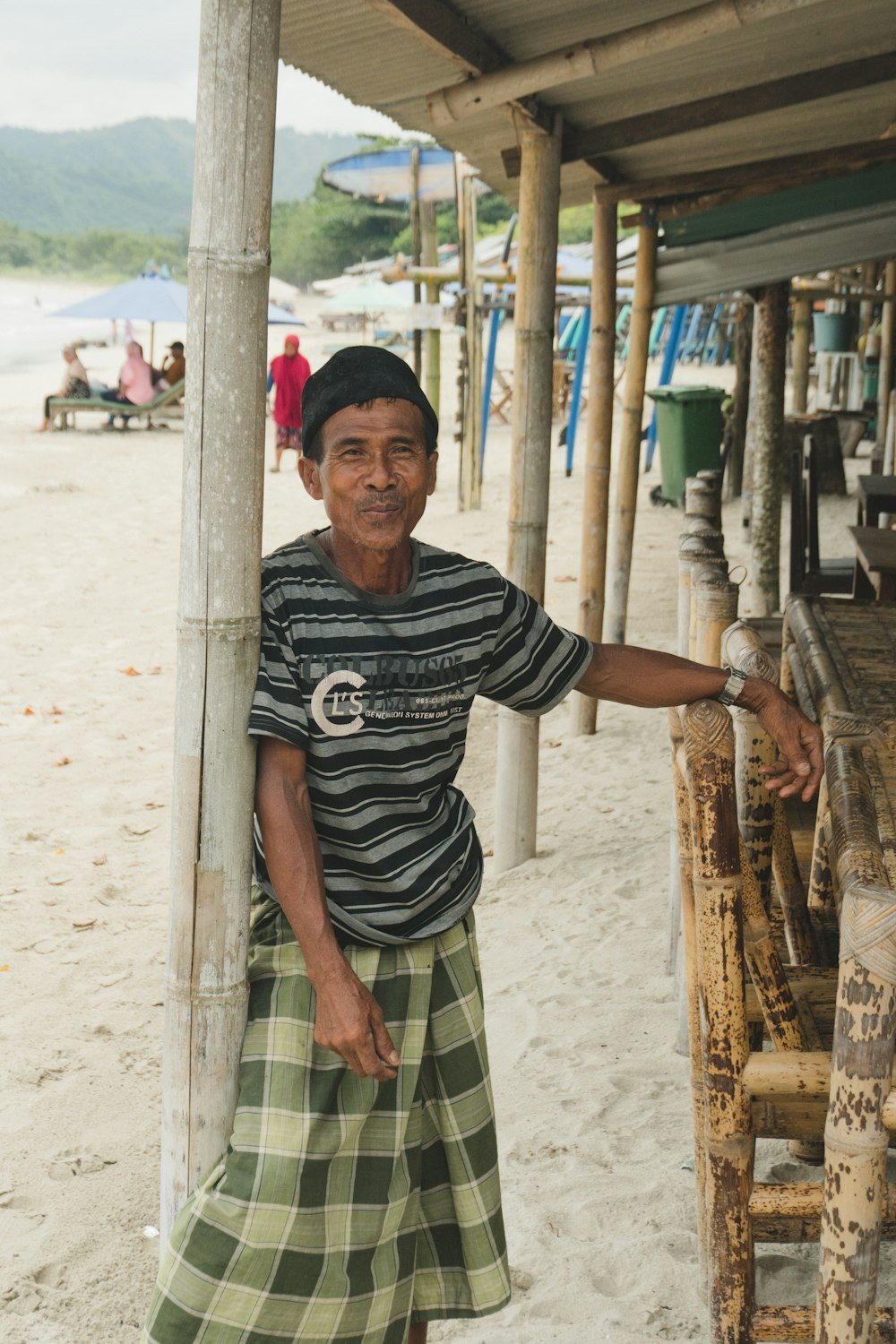 a man standing next to a wooden bench on a beach