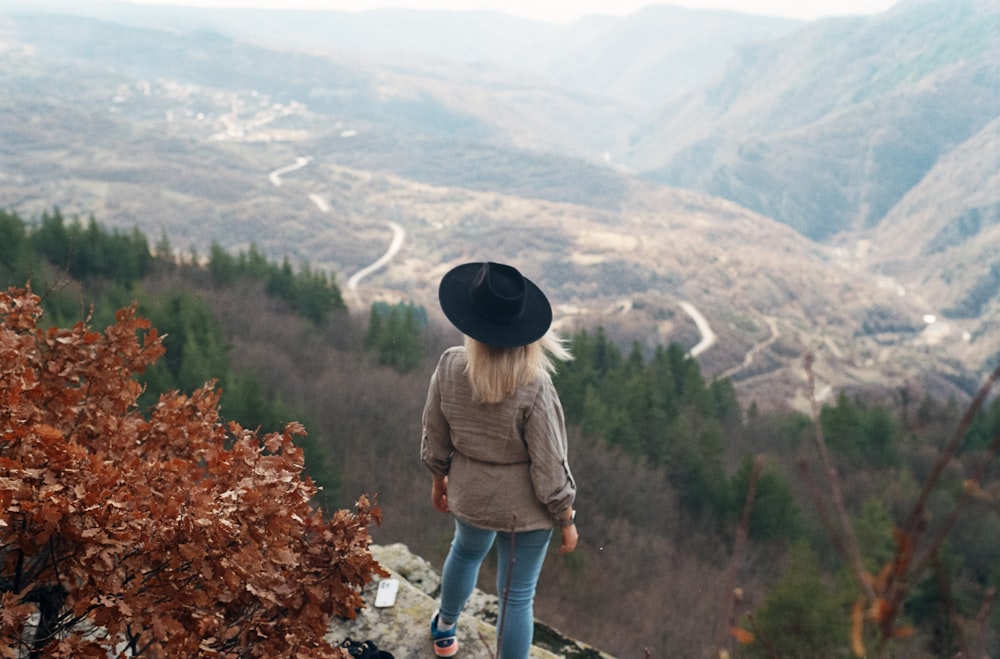 a woman standing on top of a mountain overlooking a valley