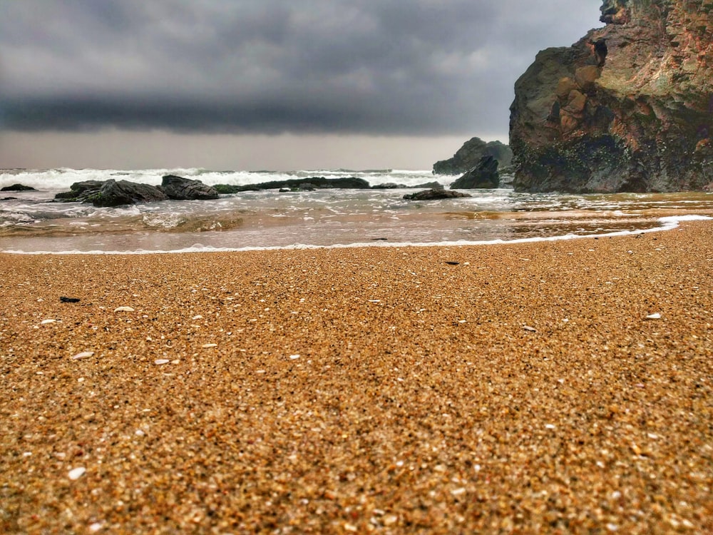 a sandy beach next to the ocean under a cloudy sky