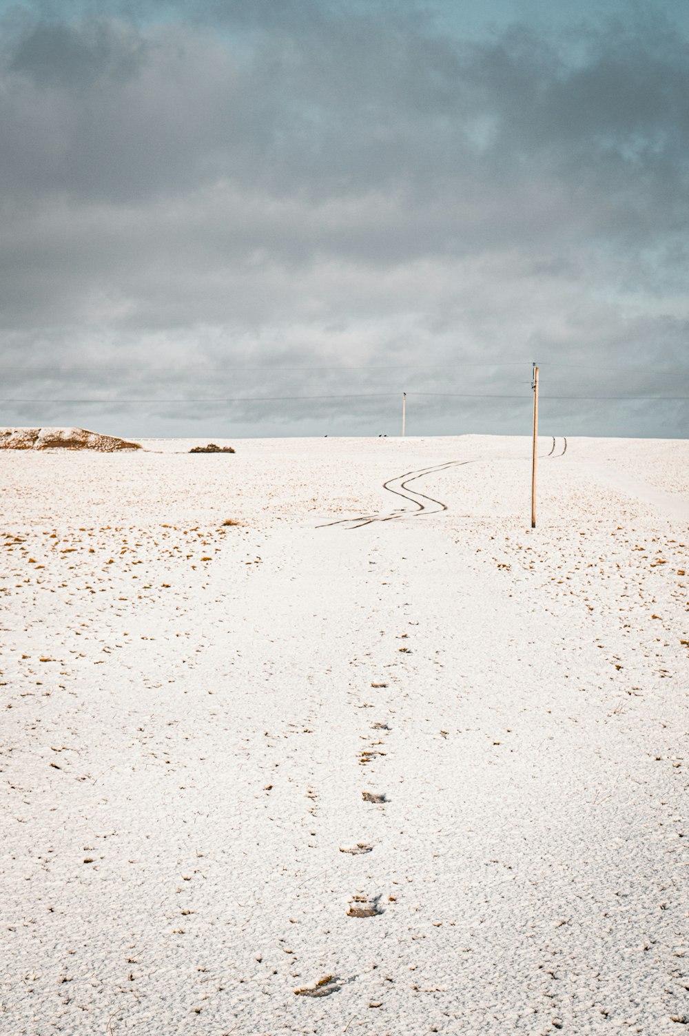 a beach with footprints in the sand and a pole in the foreground