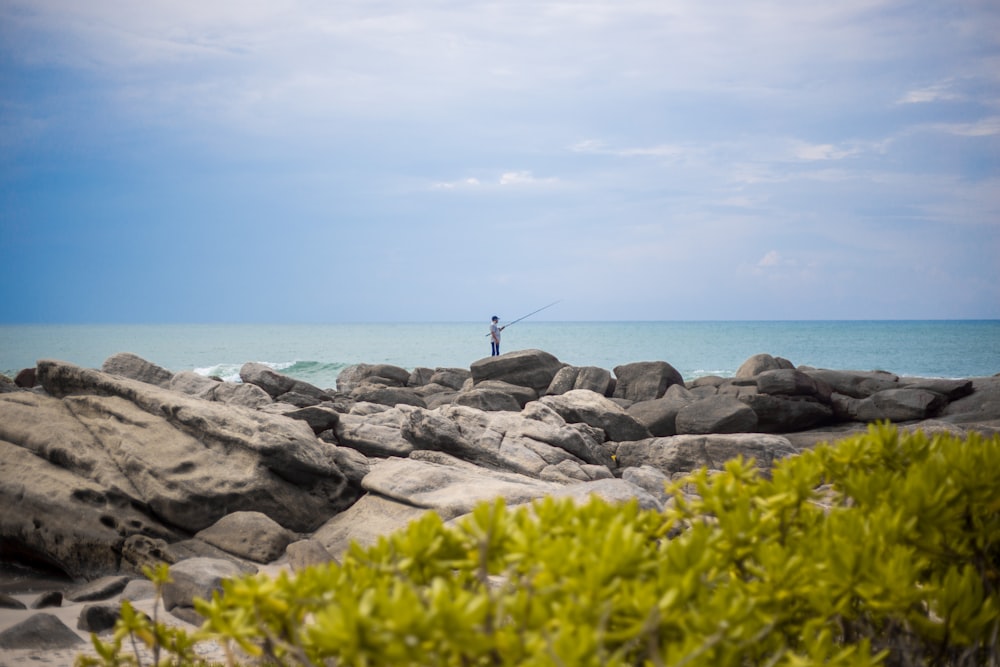 a person standing on a rock with a fishing rod