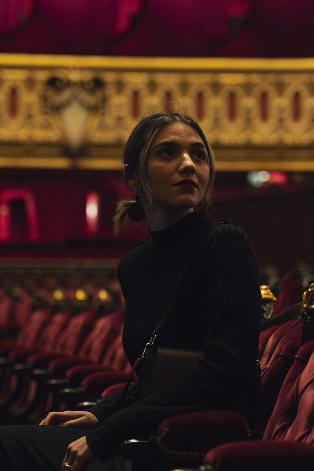 a woman is sitting in a theater with red seats