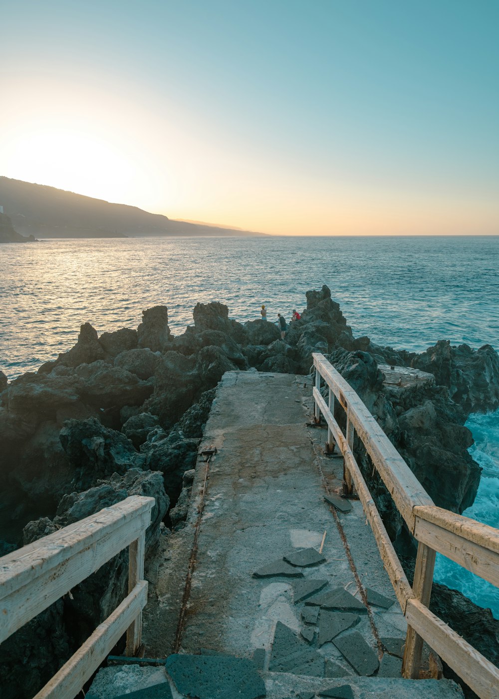 a wooden walkway leading to the ocean at sunset