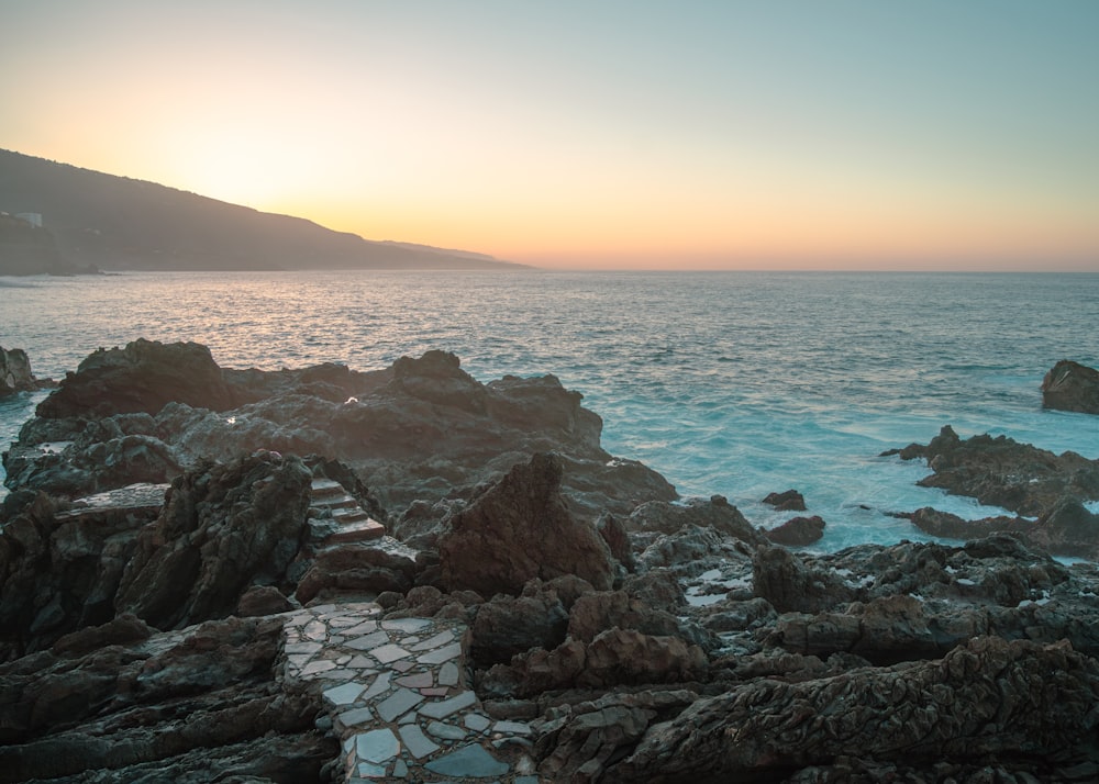 the sun is setting over the ocean and rocks