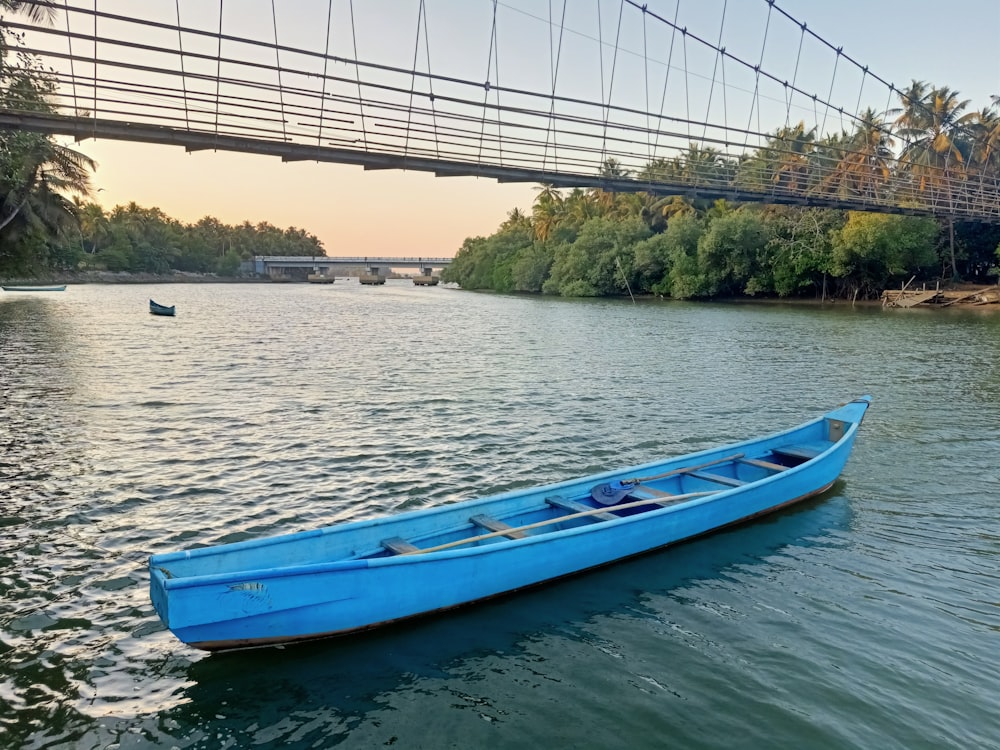 a blue boat floating on top of a river under a bridge