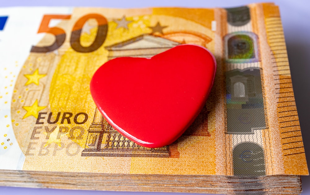a red heart sitting on top of a pile of money