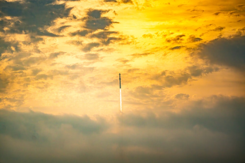 a plane flying through a cloudy sky at sunset