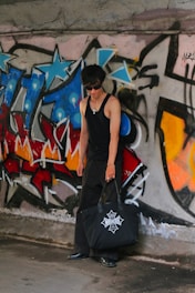 a man with a black bag standing in front of a graffiti covered wall
