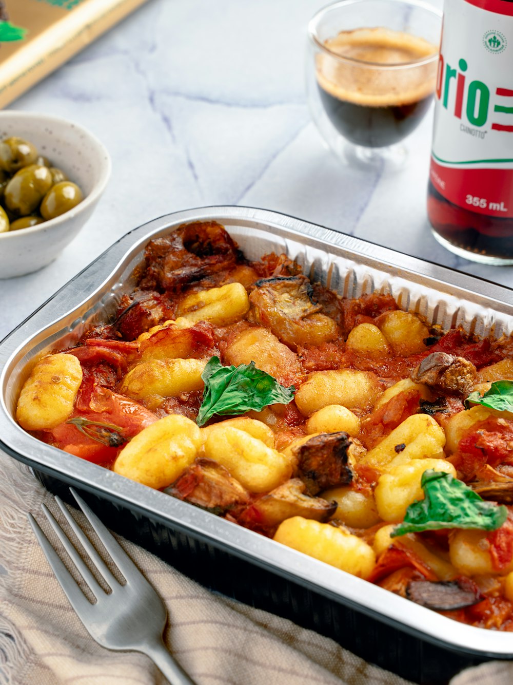 a casserole dish with tomatoes, olives, and meat