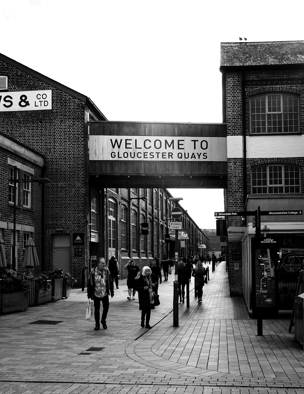 a black and white photo of people walking under a welcome sign
